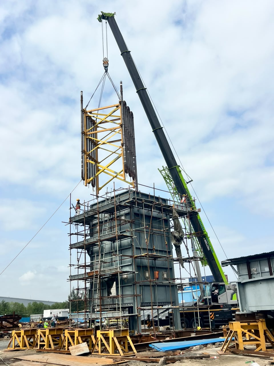 Crane lifting a yellow structural frame over a scaffolded base